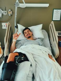 Kai Havertz in a hospital bed wearing a knee brace, giving a thumbs-up.