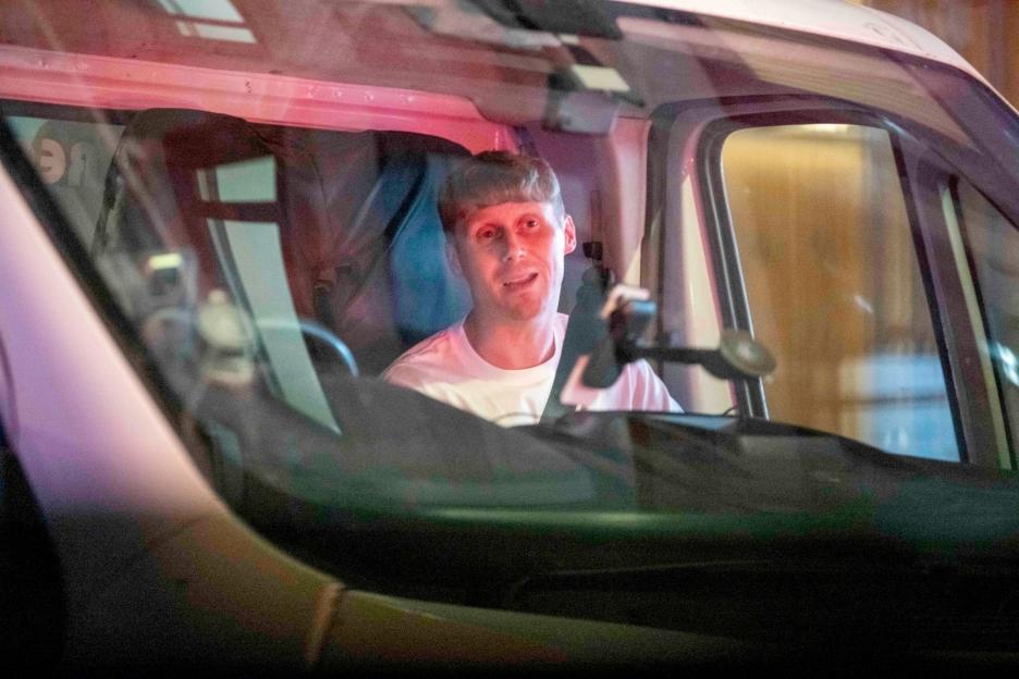 Actor Jamie Borthwick sitting in the driver's seat of a car, seen through the windshield.
