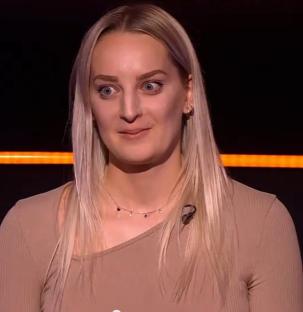 Screenshot of a blonde woman wearing a taupe top.