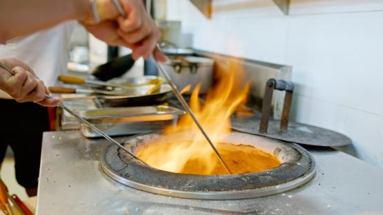 Chef using tongs to remove naan bread from a tandoor oven.