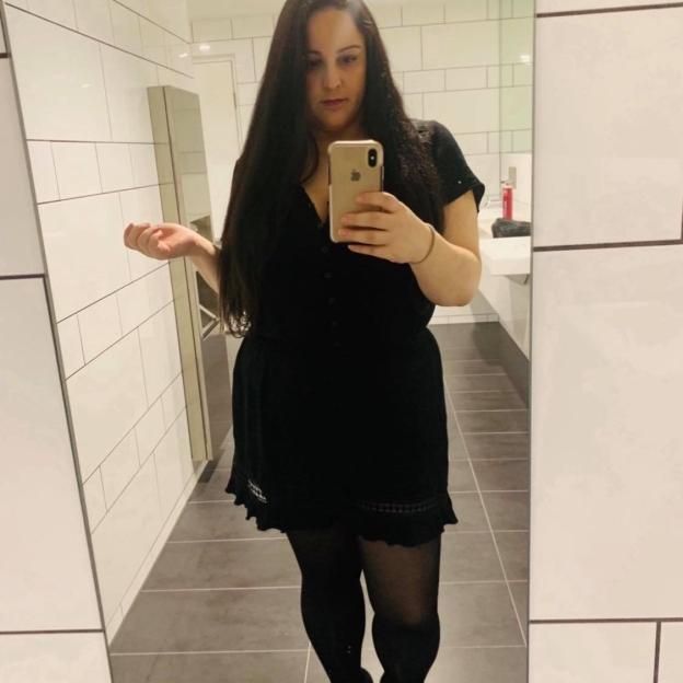 Woman in black dress taking a selfie in a bathroom.