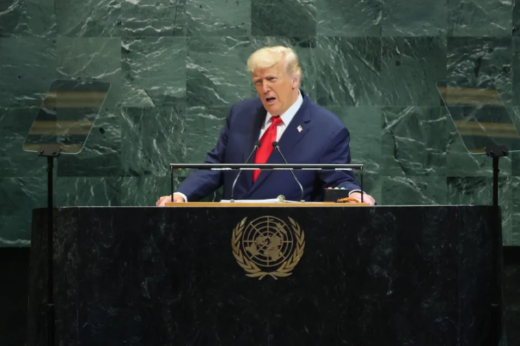 Donald Trump speaking at a podium with the UN logo.
