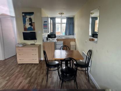 Interior view of an abandoned holiday park apartment, showing a small kitchen, dining table with chairs, and a dresser with a TV.