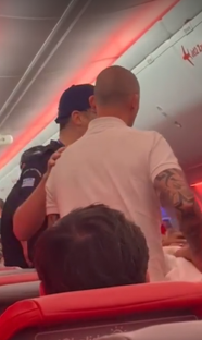 Two men on an airplane; one is bald and has a tattoo.