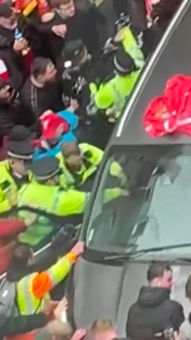 Police officers subduing a person in a car surrounded by a crowd.