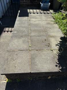 Dirty paving slabs with weeds growing in the cracks.