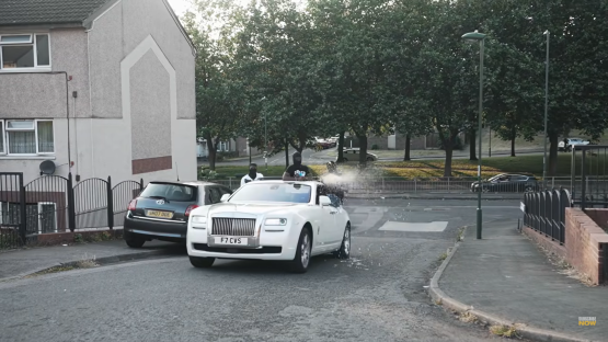 Screenshot of a music video showing men in a white Rolls Royce spraying champagne.