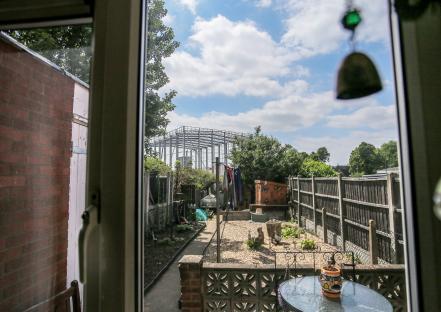 View from a window of a backyard with a large metal warehouse frame under construction in the background.