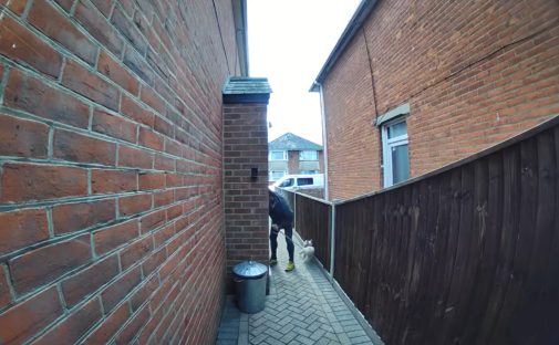 Person walking a dog down a narrow brick alleyway.