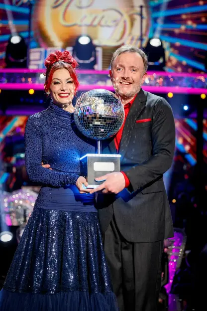 Two people holding a "Strictly Come Dancing" trophy.