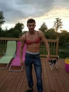 Man wearing a bra and jeans on a deck.
