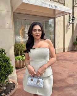 Woman in white tweed dress and Dior handbag in front of Dior store.