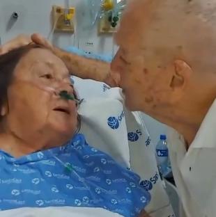 A husband kisses his wife in a hospital bed.