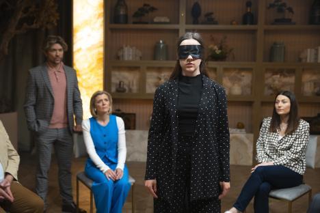 A blindfolded woman stands in front of three seated adults during a scene from Coronation Street.
