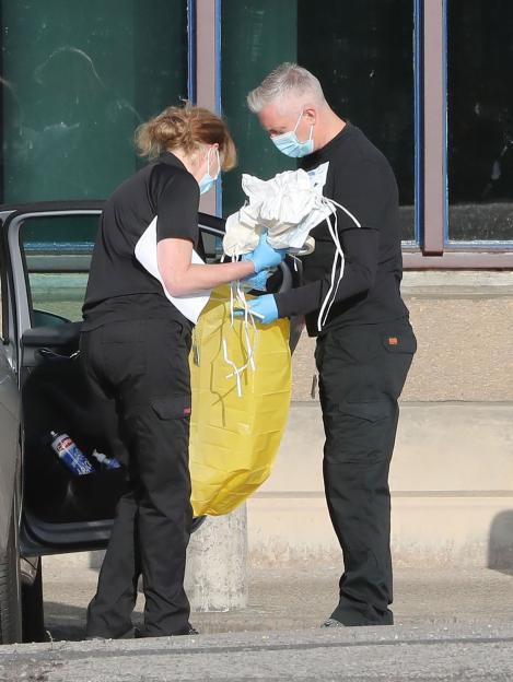 Two forensic officers in masks and gloves handling evidence in a yellow bag.