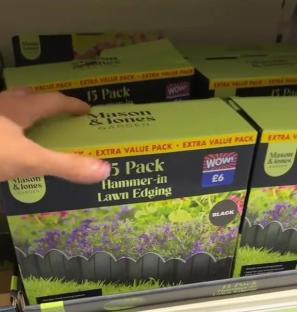 A hand picks up a 5-pack of black hammer-in lawn edging from a store shelf.