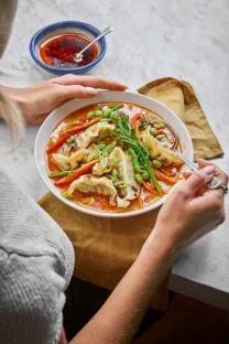 Person eating a bowl of soup with dumplings and vegetables.