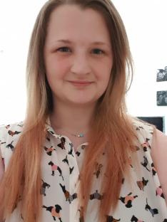 Woman with long light brown hair wearing a dog-print blouse.