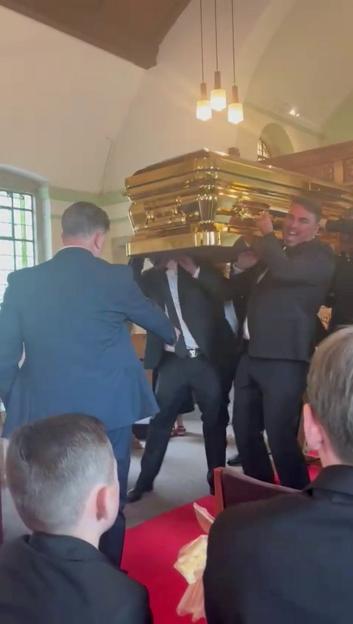 Pallbearers carrying a gold coffin into a church.