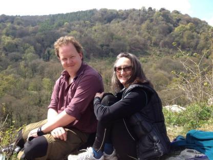 Photo of a man and woman sitting outdoors, overlooking a wooded hillside.