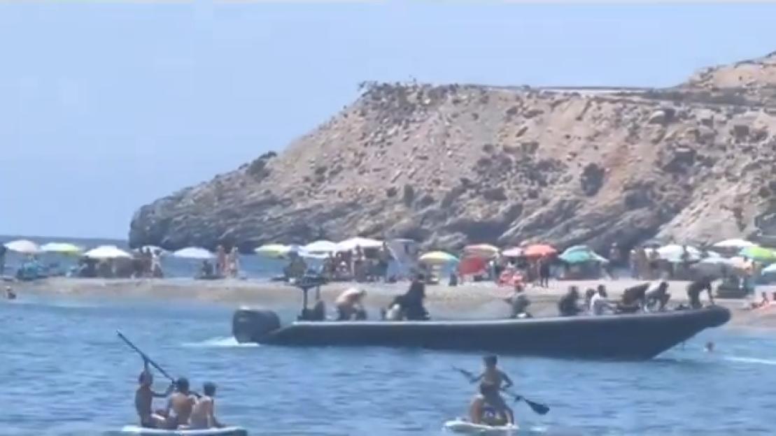 A boat arriving at a beach with many people.