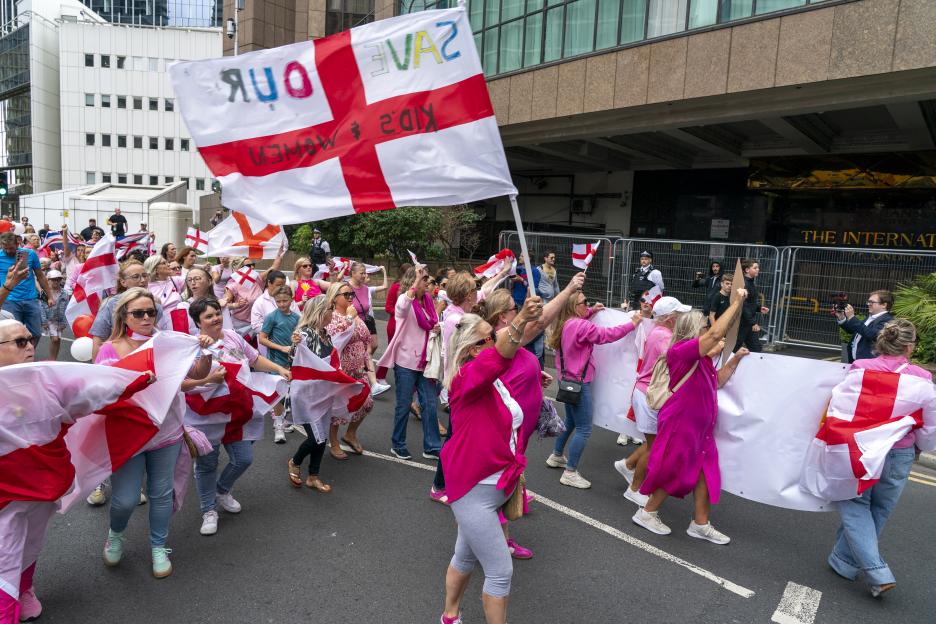 Protestors outside a hotel carrying flags that read "Save Our Kids & Women".
