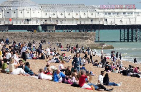 Crowds of people relaxing on Brighton Beach with the pier in the background.