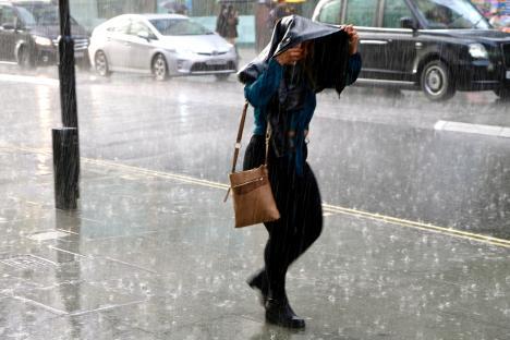 Woman walking down a city street in heavy rain, using a jacket as a makeshift shelter.