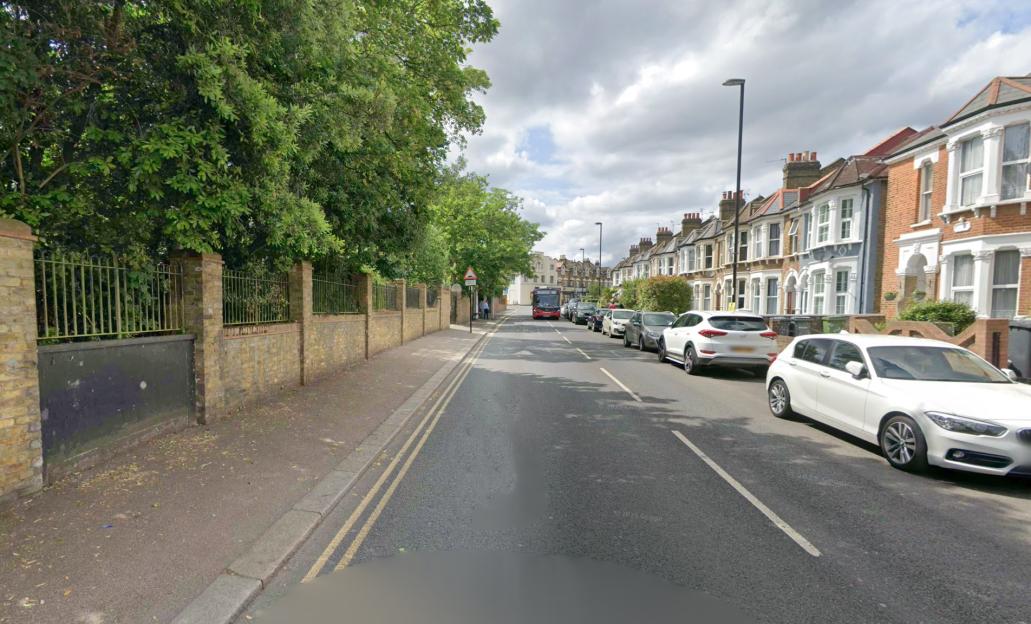 Residential street with parked cars, a bus, and brick houses in Hither Green Lane.