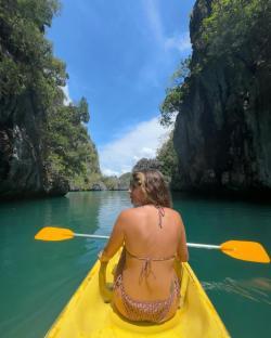 Woman kayaking through a narrow channel between limestone cliffs.