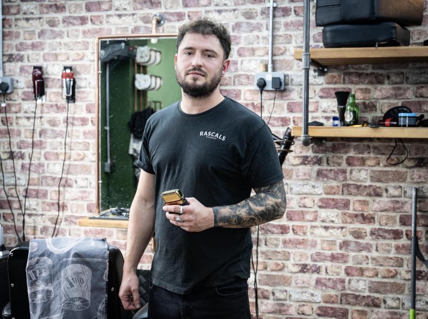 Barber Sam Pigott stands in his shop holding an electric shaver.