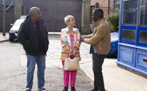 Three people talking on a street.