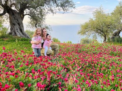 Family with two young children sitting in a field of flowers near the ocean.