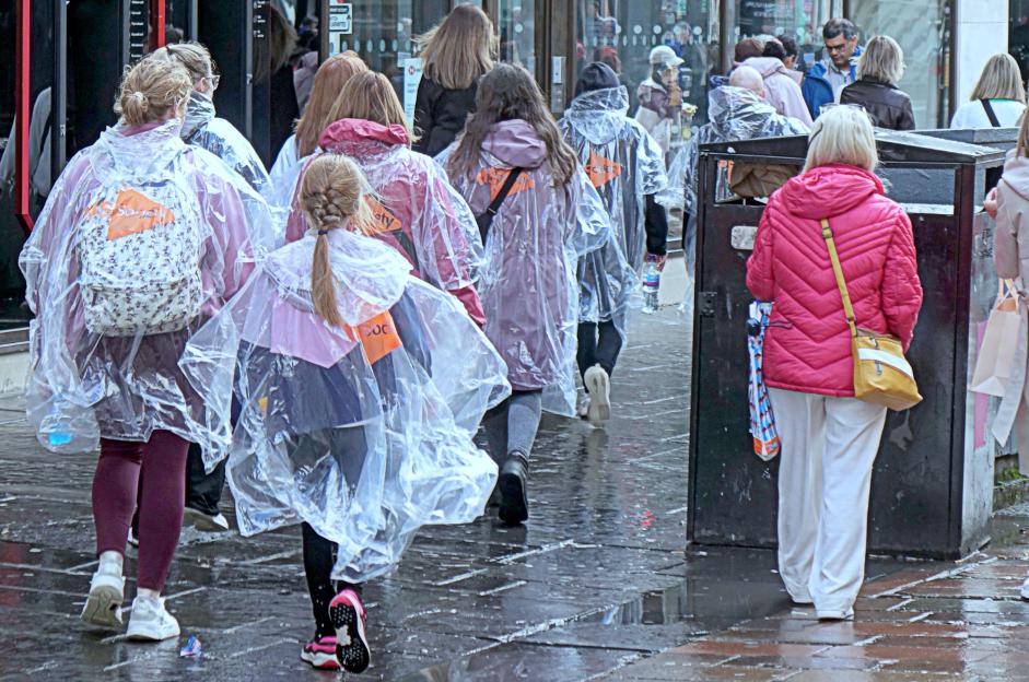 People wearing rain ponchos walk on a rainy city street.