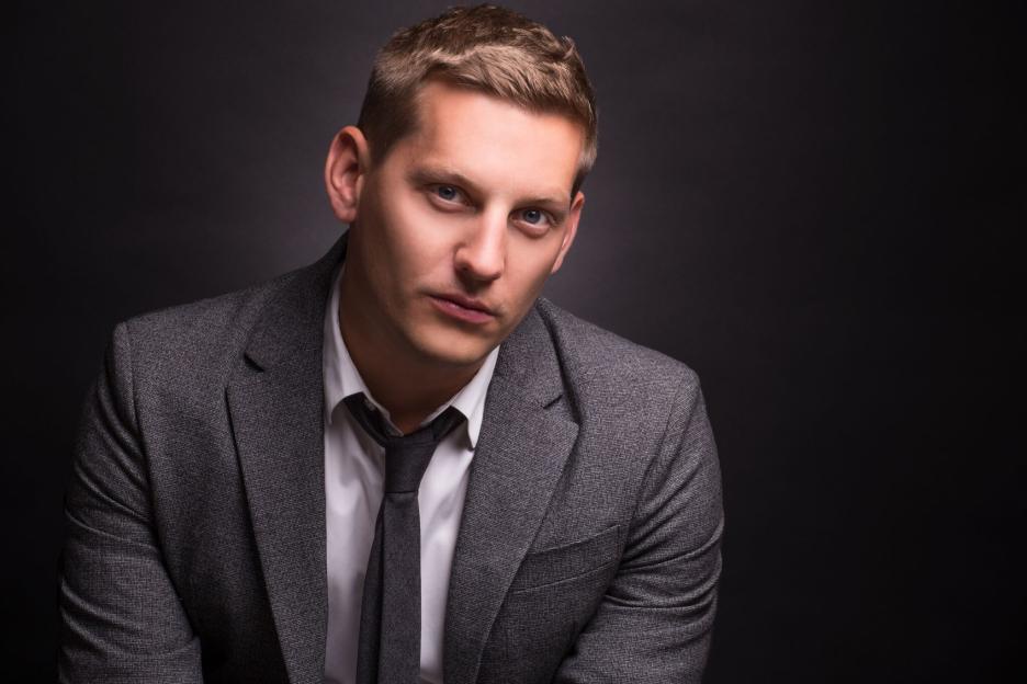James Sutton, actor who plays John Paul McQueen, in a gray suit and tie.