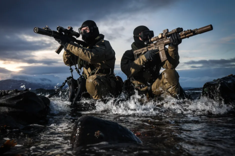 Two soldiers in camouflage gear wade through water, aiming rifles.