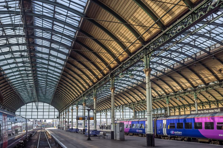 Hull Paragon Interchange railway station, with a curved glass and metal roof and trains on either side of the platform.