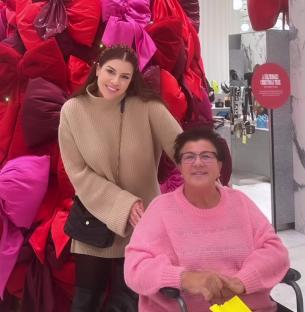 Two women posing in front of a large Christmas tree made of bows.