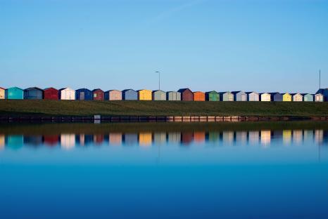 Colorful beach huts reflected in a calm lake.