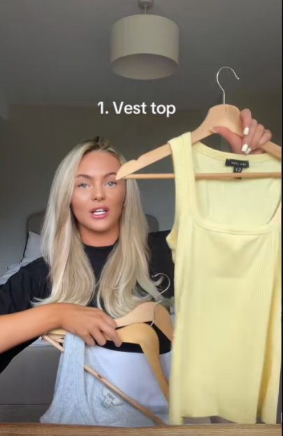 Woman holding up a yellow vest top on a hanger.