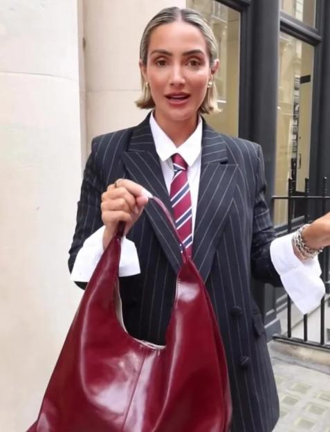 Frankie Bridge wearing a pinstripe blazer and a striped tie, holding a red handbag.