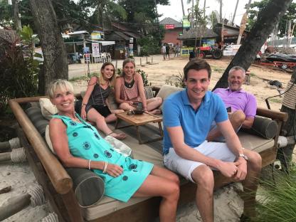 Family sitting on a daybed on a beach in Thailand.