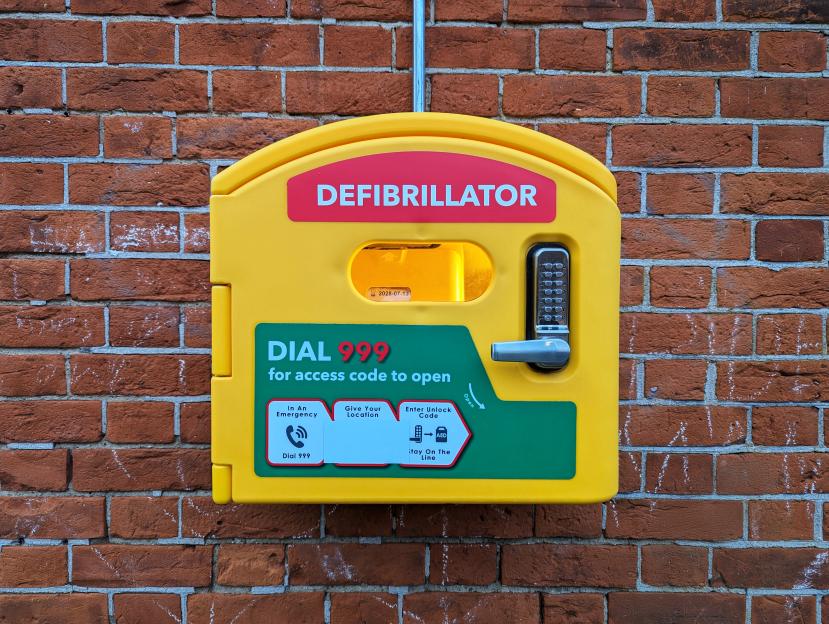 Yellow defibrillator cabinet mounted on a brick wall.