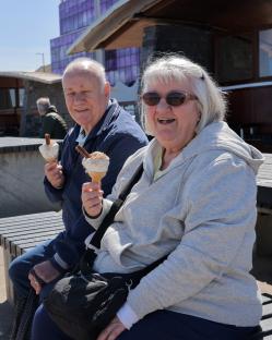 Older couple enjoying ice cream cones on a bench.