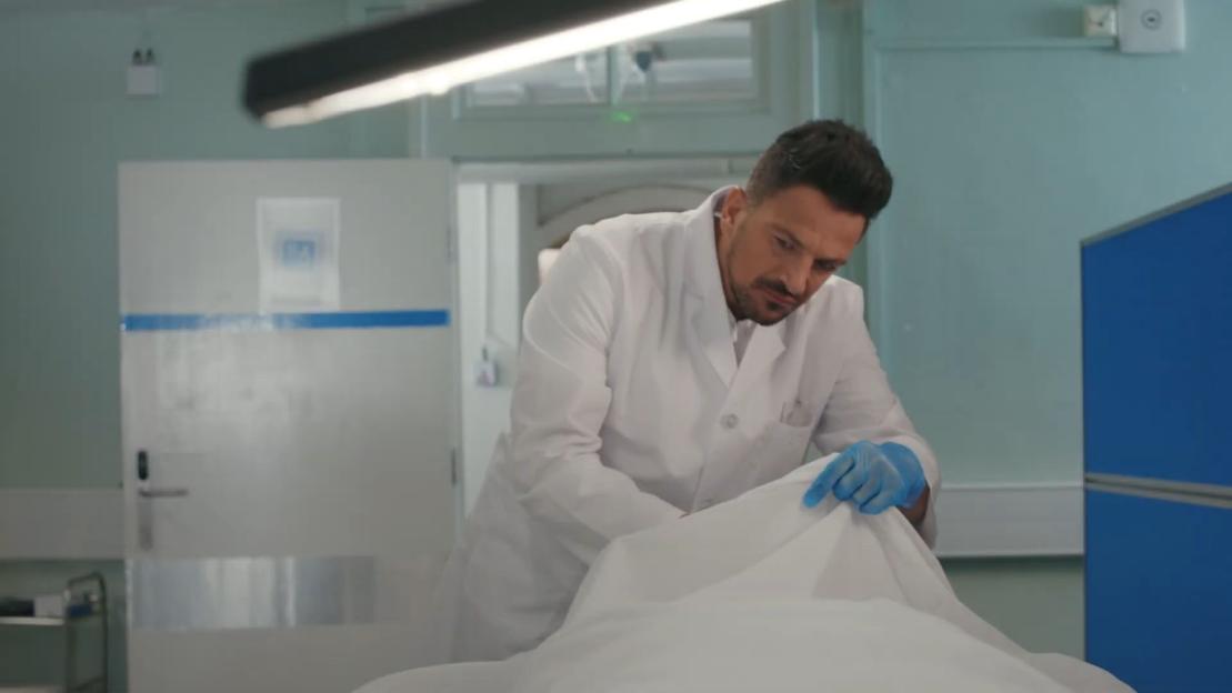 A doctor in a white coat prepares a body bag.