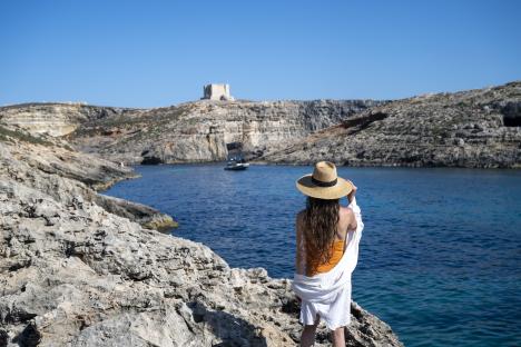 Woman in a straw hat overlooking a blue lagoon from a rocky cliff.