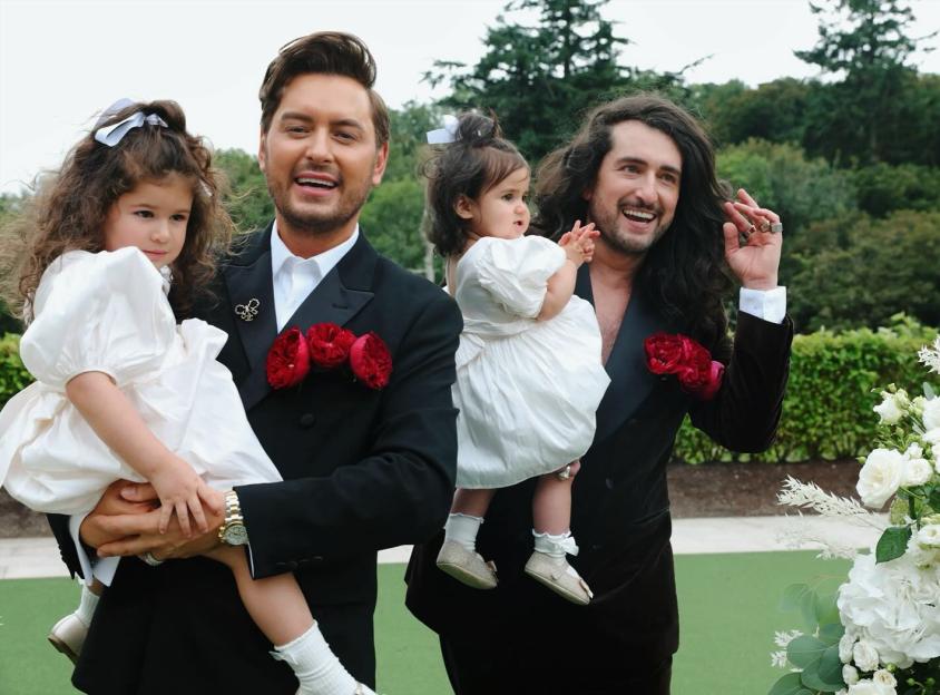 Two men in tuxedos holding young girls in white dresses.