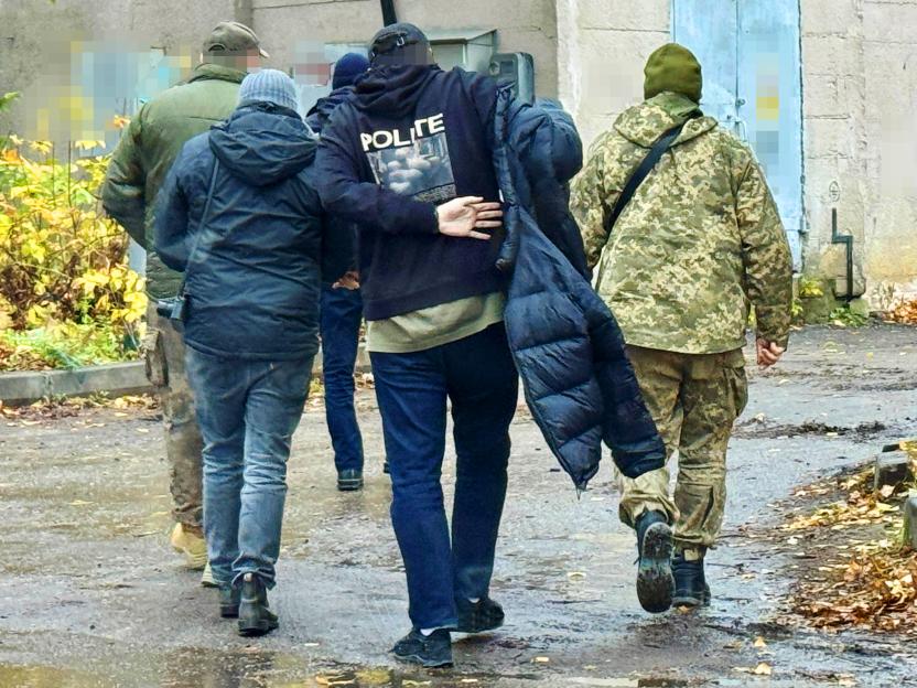 Four men in civilian and military clothing, with faces blurred, walk away from the viewer.