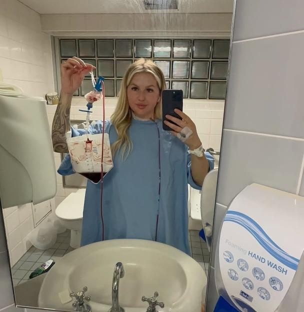 Woman in hospital gown taking a selfie while holding up a bag of radioactive iodine.