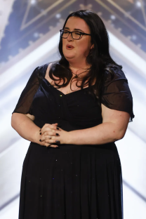 Woman in black dress and glasses speaking.